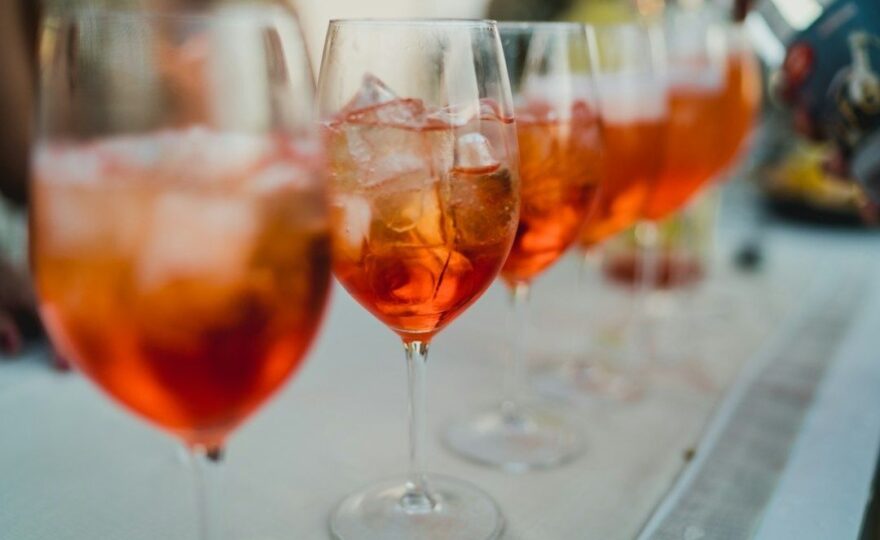 Kolme oranssia aperitiivicocktailia viinilaseissa pöydällä